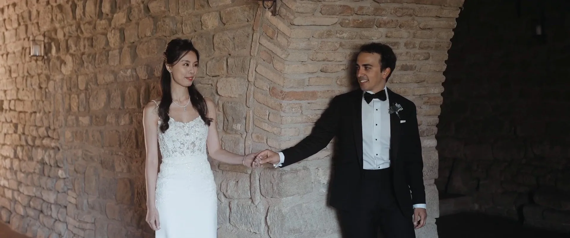 Andrea and Chloe hand in hand in the stone hall of Castello di Rosciano