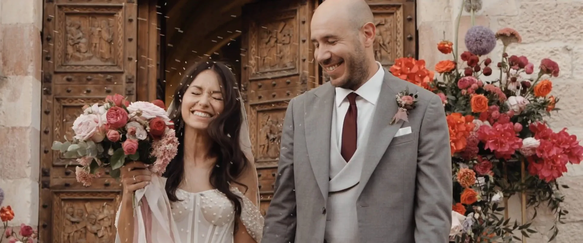Edoardo and Gloria smiling in front of the flower-covered doorway, a frame from their film