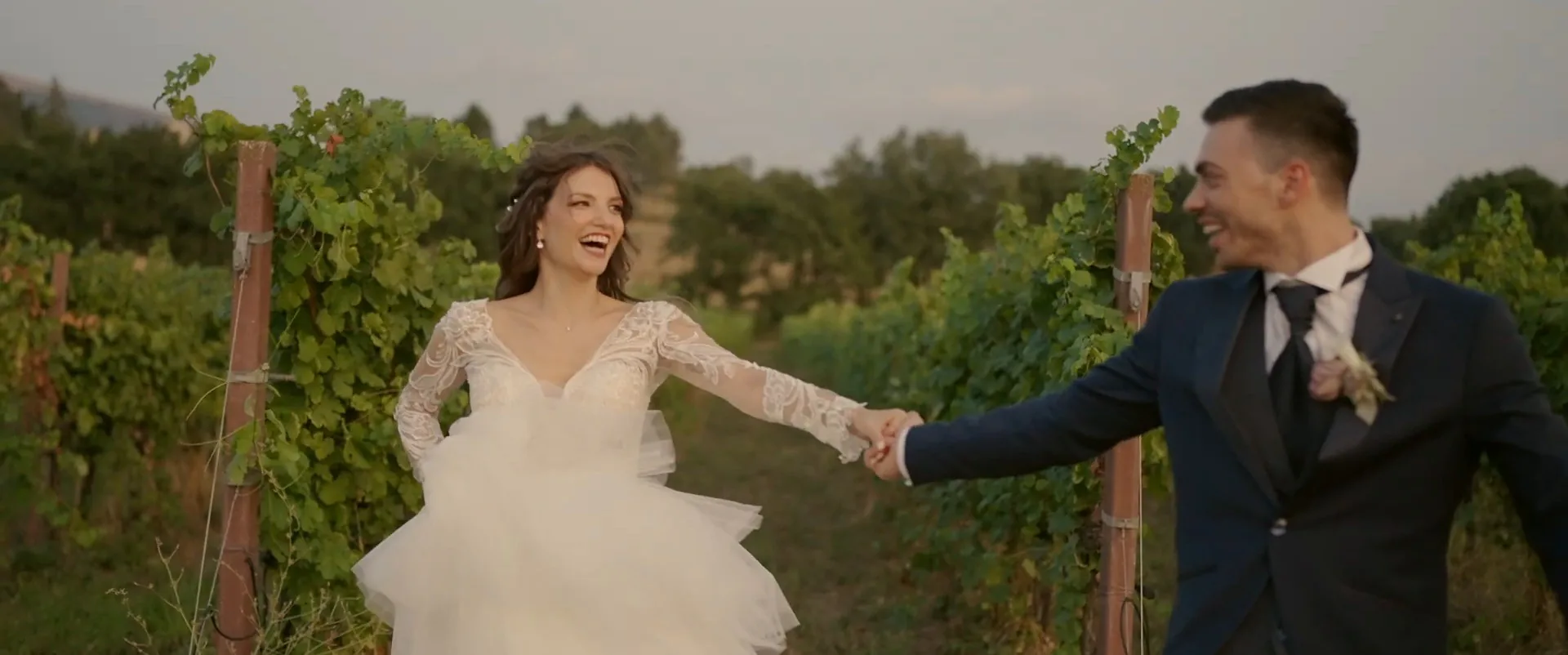 Giada and Marco holding hands among the vines at sunset, a frame from their wedding film