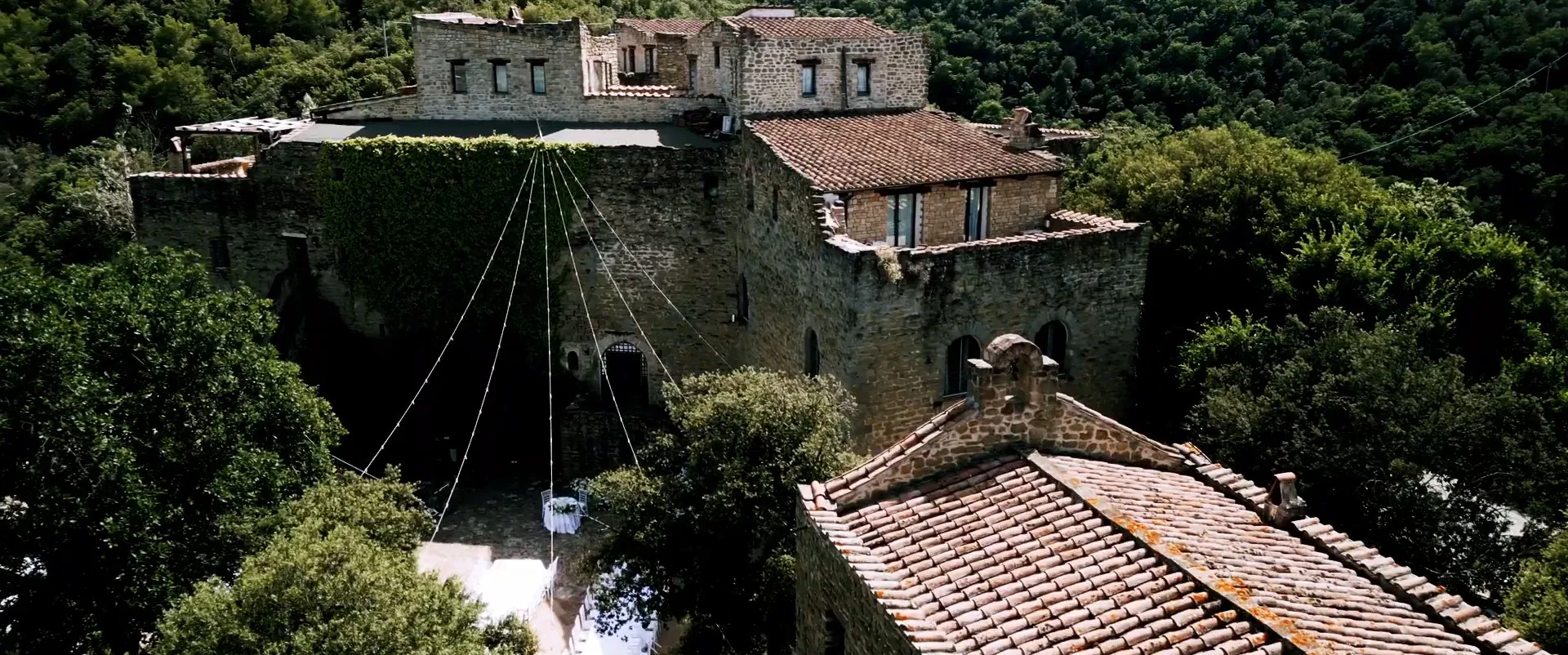 The walls and rooftops of Castello di Rosciano from above, with lights strung over the courtyard, a frame from Gianni and Sophie’s wedding film