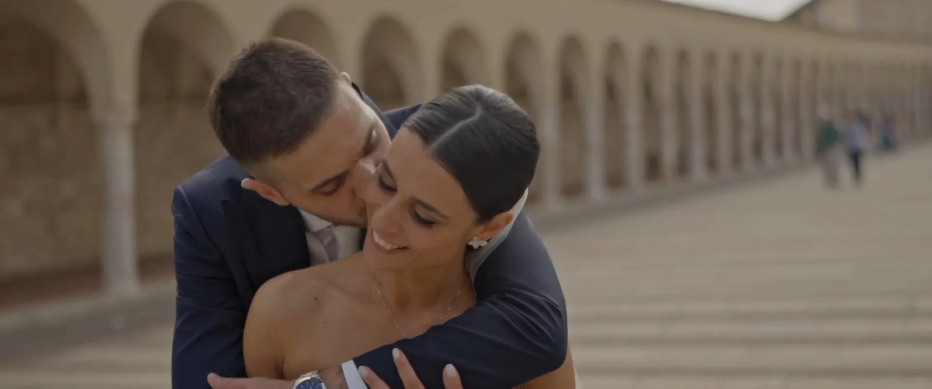 Giulia and Alessandro embracing beneath the colonnades of the Basilica of Saint Francis