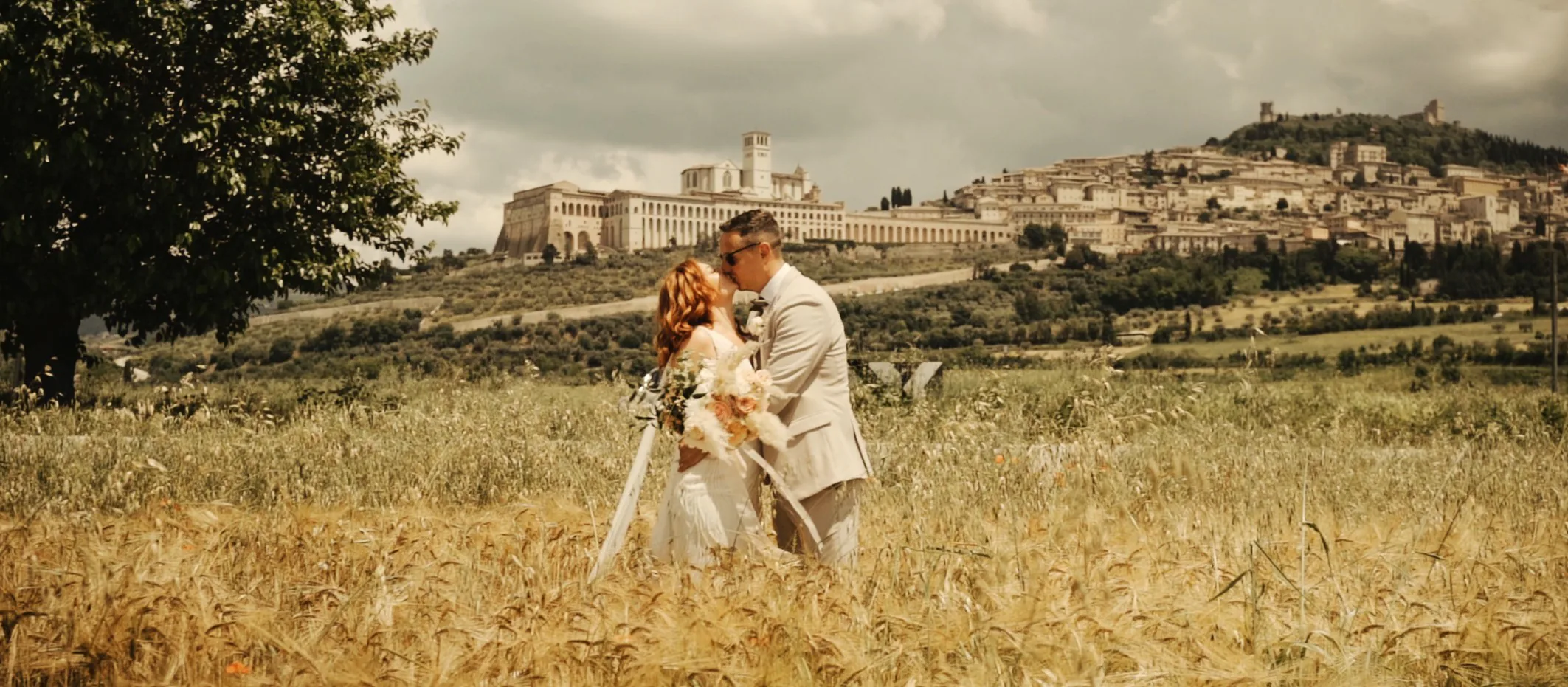James and Stacey walking through a wheat field with Assisi behind them
