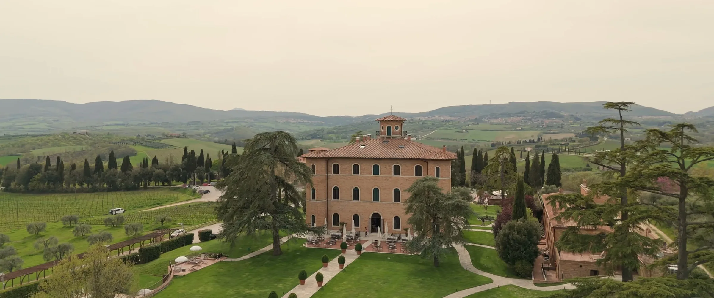 The brick villa of Poggio alla Sala among gardens, cypresses and vineyards, seen by drone, a frame from a Chinese destination wedding film in Tuscany