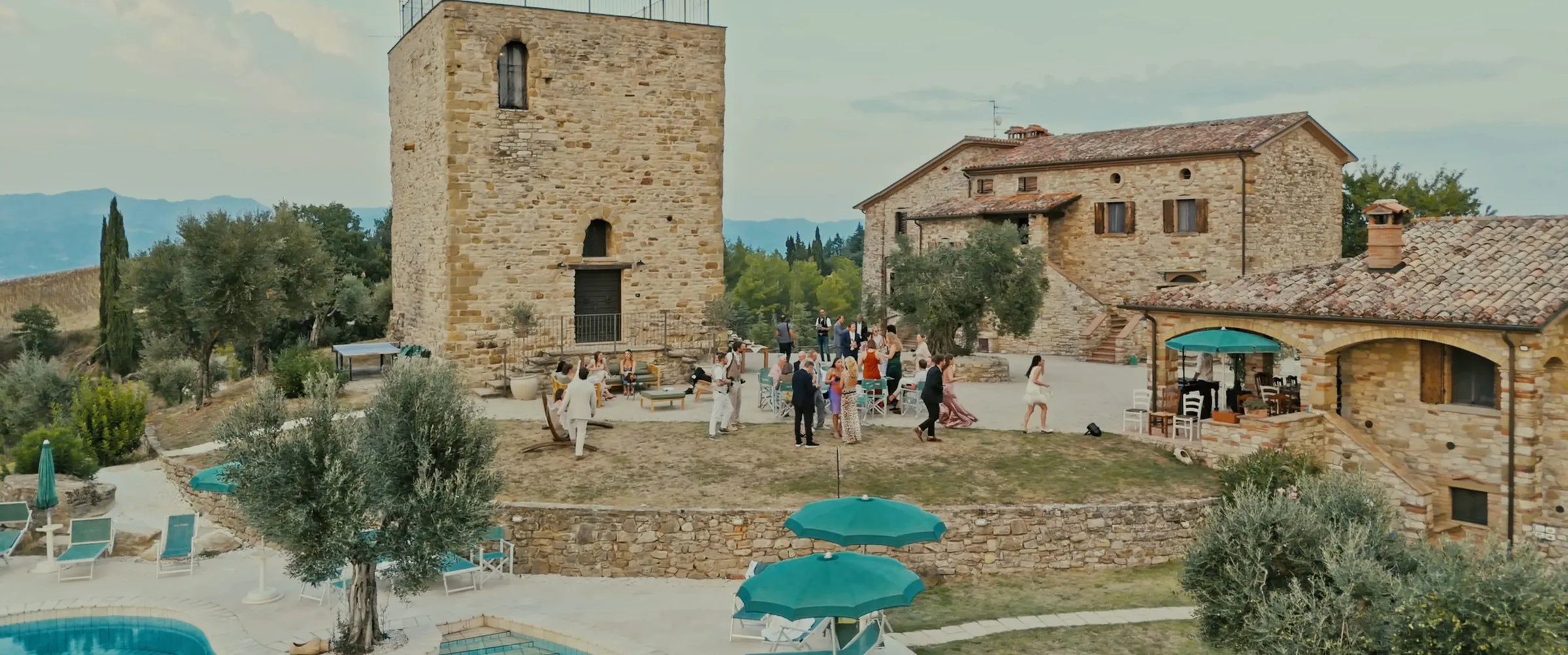Guests gathering in front of the medieval tower and farmhouse at La Torre di Celle, a frame from Tyler and Jaime’s wedding film