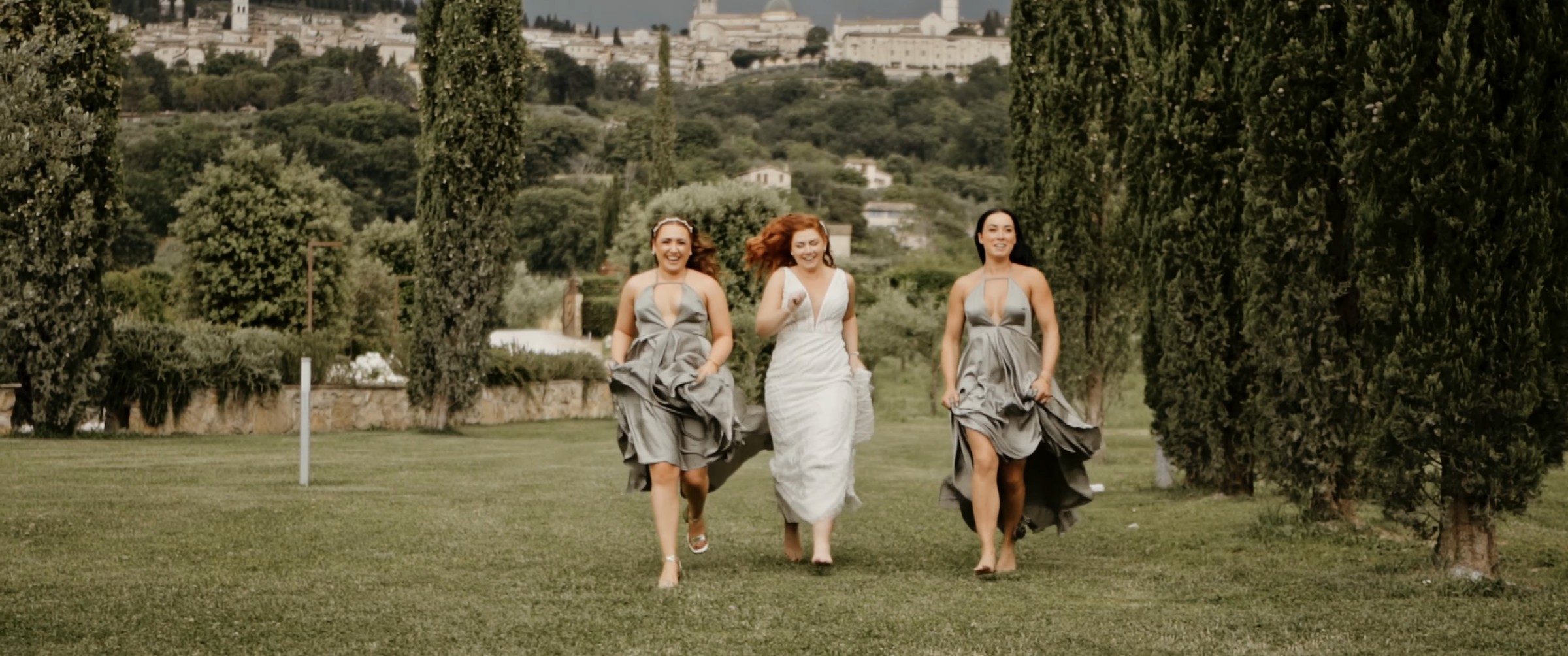 Le damigelle corrono nel giardino tra i cipressi alla Tenuta di San Masseo, con Assisi sullo sfondo, fotogramma dal film di James e Stacey